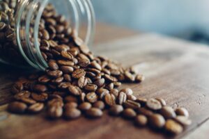 Whole roasted coffee beans poured out on the counter top for a jar