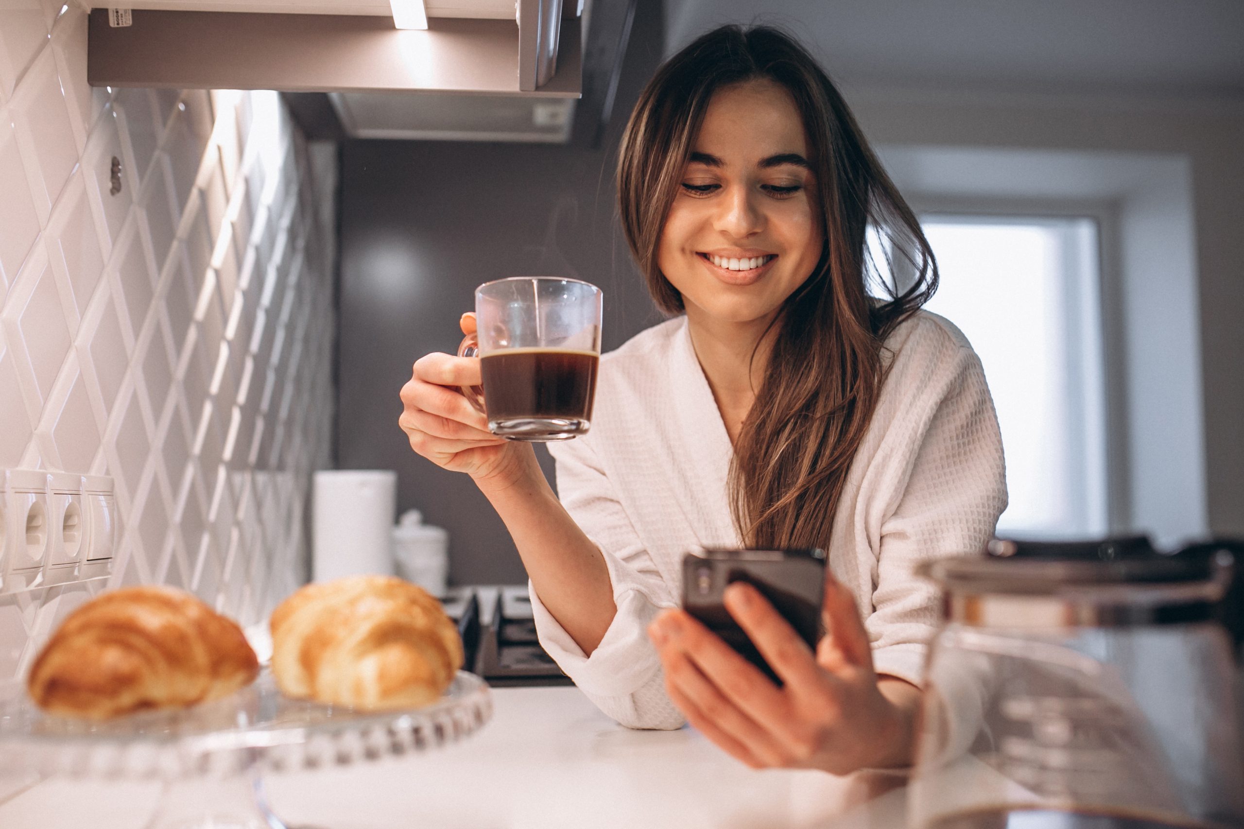 Lady enjoying cup of coffee reading up her phone in the kitchen